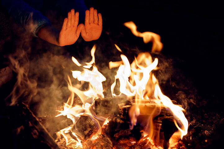 eine Person wärmt ihre Hände am Lagerfeuer