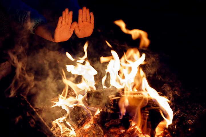 fair-finance Feuer soziale Verantwortung eine Person wärmt ihre Hände am Lagerfeuer